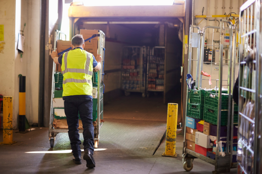 An employee in a yellow high vis pushing a quiet mark certified roll cage.